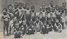 A group of 15 boys, 10 standing and five squatting. Most appear naked. All have prominent pot-bellies but ribs obviously showing, a common symptom of malnutrition.