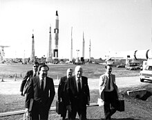 Black-and-white photo of a group of individuals at the Kennedy Space Center with the rocket garden behind them
