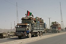 Two trucks full of household belongings, one with a black, red and green Afghan flag