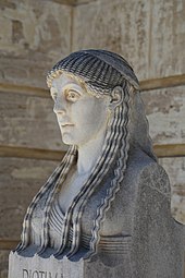 Bust of a woman; she has long braided hair
