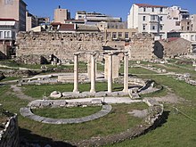 Photograph of Ancient Greek ruins, with modern buildings behind.
