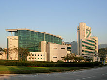 A building complex with a wide glass building on the left and a tall and medium height office building on the right.