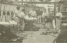 A group of men conducting loading drills stand around a large gun.