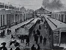 Several workers stand among trains and buildings with shovels in their hands