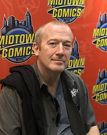 Ennis seated in front of a banner with the Midtown Comics logo