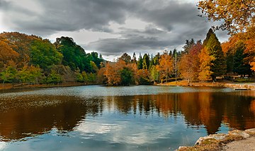 Photographie d'un lac espagnol en automne comme en témoigne les arbres à la teinte orangée, le ciel est couvert de nuages gris