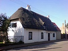 White thatched cottage single storey 3 windows 1 front door 1 attic window chimney No front garden