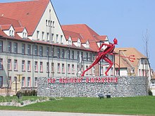 La statue d'un diable rouge avec un bâtiment militaire en arrière-plan.
