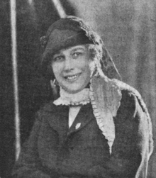 Grainy portrait photo of a smiling woman wearing a hat.