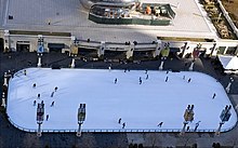 An ice skating rink with a few skaters and a large metallic sculpture in the background