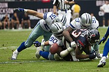 Photograph of defensive players tackling an offensive player who has just lost control of the football
