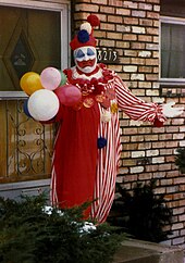 A heavy-set man in a clown costume, with balloons and waving
