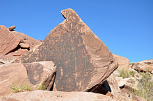 Images of animals, people, and geometric figures incised on the dark vertical face of a large rock