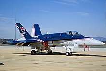 Photo of a modern fighter aircraft parked on tarmac. The top of the aircraft is painted blue, while the remainder is grey.