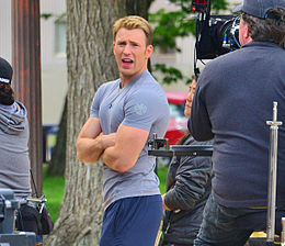 Candid photo of Chris Evans, wearing workout clothing in-character as Captain America, standing in front of a camera