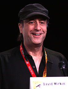 A man wearing a cap smiles as he looks into the distance.