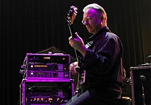 Robert Fripp ergonomically plays electric guitar while sitting in a posture developed through years of application of the Alexander Technique.