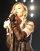 A blond woman dressed in a jeweled dress sings to a microphone