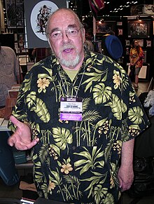 A man in his late sixties. He has a beard, glasses, and is wearing a Hawaiian shirt.