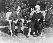 Herbert and Lou Hoover sit beside one another in wicker chairs