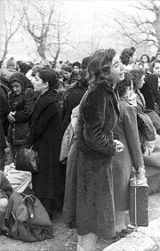 A group of women with bundes and suitcases are standing together while one woman weeps.