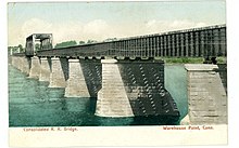 A photograph of a railroad bridge crossing a river; the piers are made of stone, while the deck is made of iron.