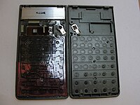 Inside a Casio scientific calculator from the mid-1990s, showing the processor chip (small square; top-middle; left), keypad contacts, right (with matching contacts on the left), the back of the LCD (top; marked 4L102E), battery compartment, and other components. The solar cell assembly is under the chip.