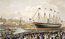 Kalabalık bir grup büyük, altı direkli ve bir bacalı, bayraklarla donatılmış kırmızı ve siyah renkli bir gemiyi izliyor.
