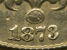 A closeup of part of an 1873 Shield nickel; the arms of the "3" curve only slightly towards each other