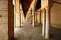 Vue intérieure du portique oriental avec, au milieu, une rangée d'arcades à colonnes de remploi. Il est couvert d'un plafond en bois à solives apparentes.