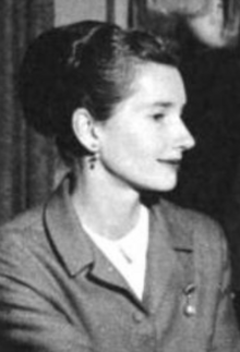 A white woman with dark hair in a bouffant updo, wearing a suit with a white blouse, photographed almost in profile