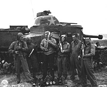 Photographie en noir et blanc montrant des soldats posant devant un char et tenant des obus.