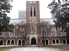 A wide, red brick building with a tower in the center and grey concrete archways spaced along the length of the building