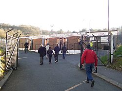 Various people walking towards the entrance to a brick-built sports stadium