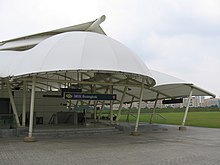 Buangkok station entrance with a white canopy. The entrance faces an open field.