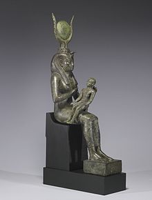 Smal statue of a seated woman, with a headdress of horns and a disk, holding an infant across her lap