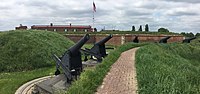 Cannons next to grassy embankment in front of brick fort above which the US flag is flying