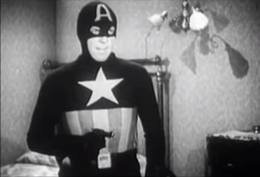 Black-and-white screencap from Captain America (1944) of Captain America in costume holding a gun