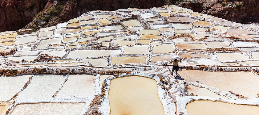 Worker carrying a sack of salt on his shoulder in Salineras (salt evaporation ponds) in Maras, Peru.