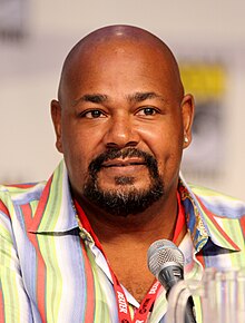 An image of a black man wearing a multi-colored dress shirt.