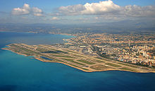 A peninsula with two runways in the middle, surrounded by water above, below and to the left; to the right and upwards is a city