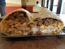 A burrito sliced in half containing carne asada, fries, cheese, and sour creme