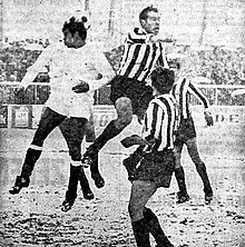 A black and white photo showing a few football players contesting for the ball in mid-air.