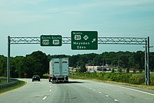 Overhead highway signage along US 220 South at the US 311 and NC 135 interchange northeast of Mayodan. The left sign indicates US 220 South and US 311 South running concurrently. The right sign indicates US 311 North and NC 135 with control cities of Mayodan and Eden. To the right of the highway, an AutoZone is apparent.