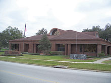 a fairly large one story brick building with a flagpole and a sign saying 'Bartow City Hall' in front