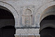 Photographie d'un panneau sculpté de la façade du portique occidental de la cour. Ce panneau en pierre est orné d'un décor symétrique de rinceaux et de fleurs, se terminant par un croissant.