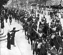 Photo noir et blanc montrant une colonne de cavaliers remontant un boulevard.