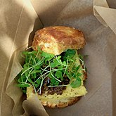 A breakfast sandwich featuring eggs, bacon jam, and microgreens on a buttermilk biscuit.