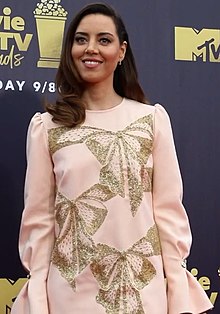 A dark brunette woman wearing a light pink dress with gold embellishments smiles