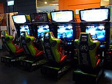 Four arcade cabinets with seats and steering wheels in a row, colored green